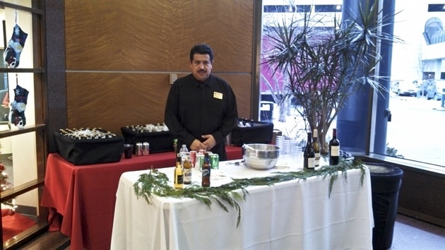 Bartender stands behind white table at a holiday party at an office