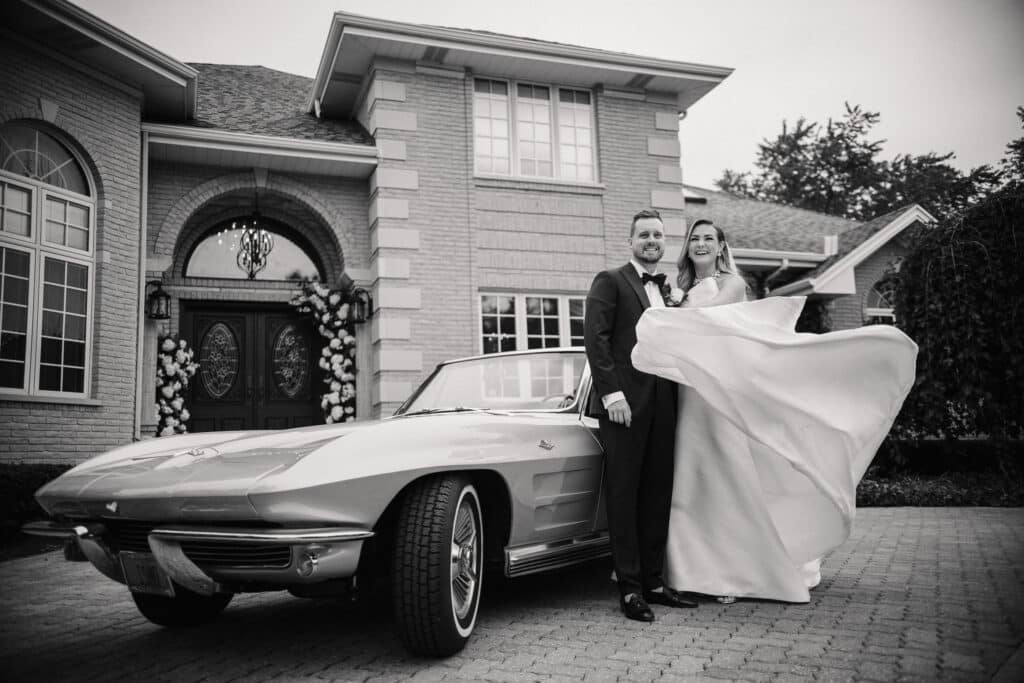 Couple with vintage car and bride flipping her dress.