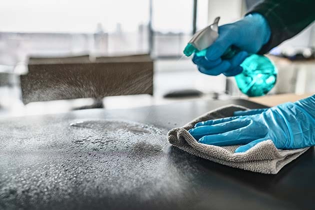 Person in blue gloves sanitizing a counter