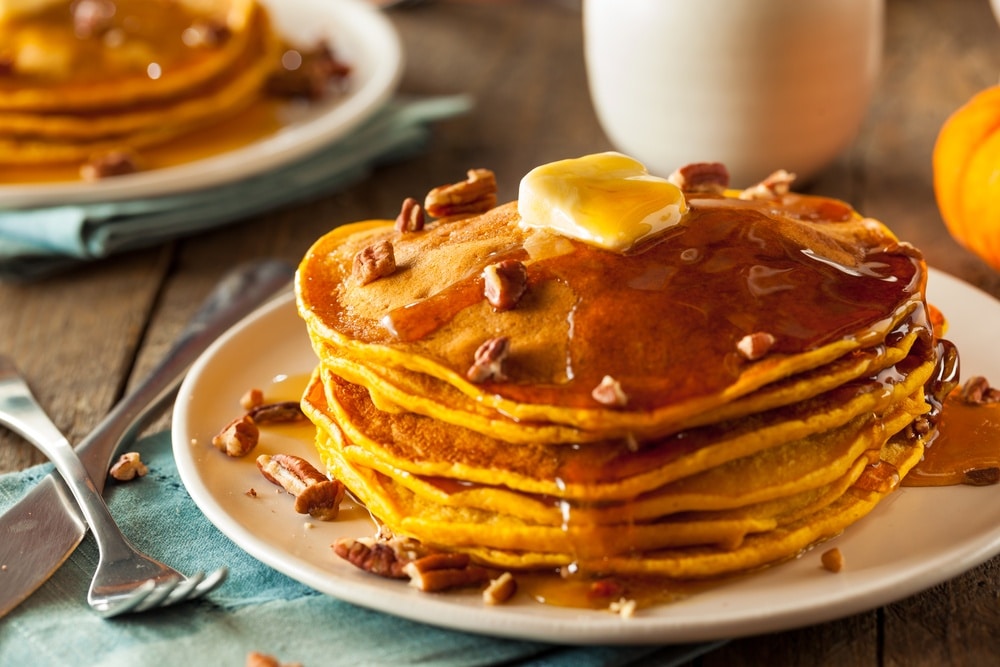 Pumpkin pancakes stacked on a plate with butter and syrup on top