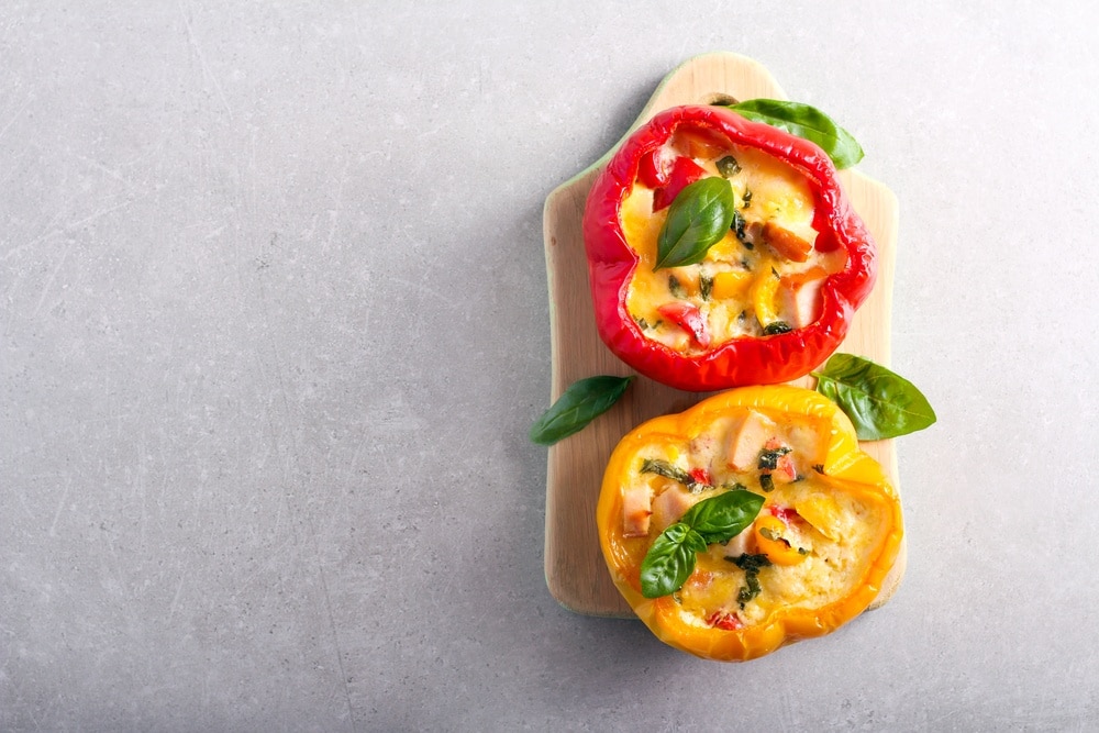 A red and yellow bell pepper stuffed with meat and cheese on a grey background