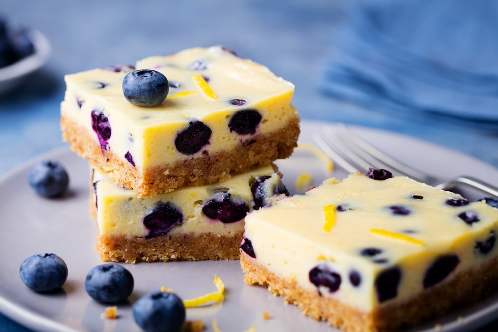 Blueberry dessert bars stacked on a plate with blueberries as a garnish